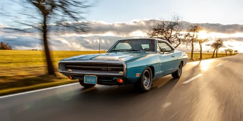 Vintage car driving down a scenic road with clear skies.