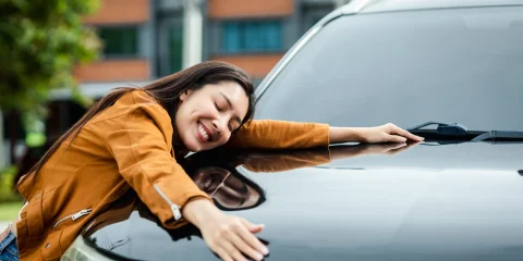 Happy woman hugging her car, showing affection and excitement.