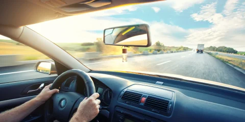 Close-up of hands gripping the steering wheel while driving on the road.