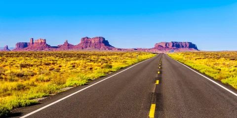 A scenic road stretching toward distant mountains, with a clear sky above.