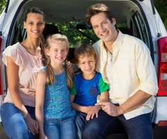 A happy family of four sitting in the trunk of a van