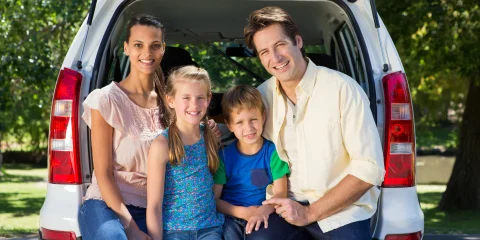 A happy family of four sitting in the trunk of a van