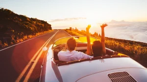 A car on the road at sunset with two people having their hands out, enjoying the view.