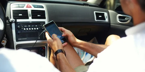 A man holding his cellphone for navigation while driving inside a car