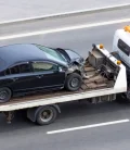 A car being towed on a flatbed tow truck along a road.