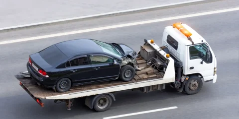 A car being towed on a flatbed tow truck along a road.