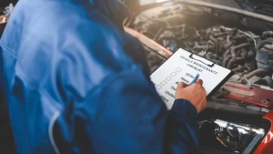 A mechanic checking a list while inspecting a car in a garage