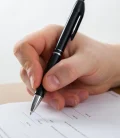 A close-up of a hand signing a car insurance contract with a pen