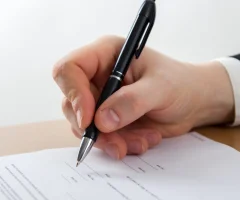 A close-up of a hand signing a car insurance contract with a pen