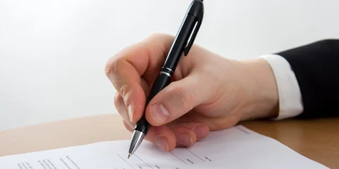 A close-up of a hand signing a car insurance contract with a pen