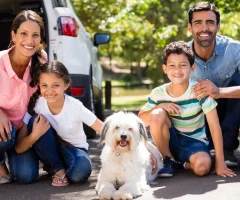 A happy family with their dog, excited and ready to embark on a road trip to Mexico in their car