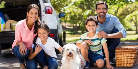 A happy family with their dog, excited and ready to embark on a road trip to Mexico in their car