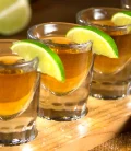 Four tequila shots lined up on a bar counter, with a vibrant lime wedge and salt