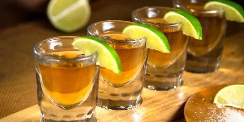 Four tequila shots lined up on a bar counter, with a vibrant lime wedge and salt