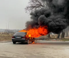 A car on fire on the side of the road, with thick smoke rising from the vehicle