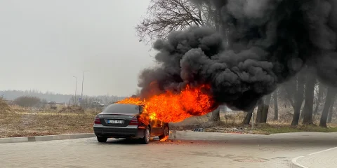 A car on fire on the side of the road, with thick smoke rising from the vehicle