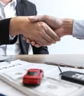 Two individuals shaking hands over a car insurance contract