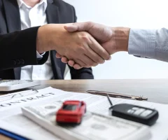 Two individuals shaking hands over a car insurance contract