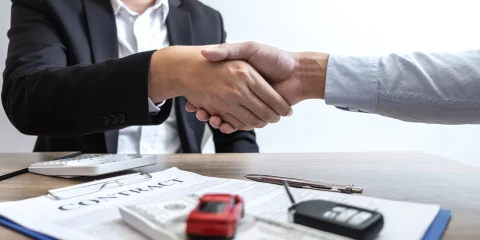 Two individuals shaking hands over a car insurance contract