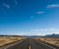 A lonely, empty road stretching into the horizon, surrounded by scenic landscapes.