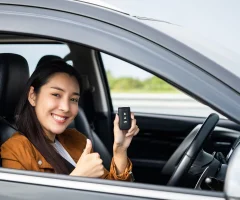 A young woman smiling and holding up her car keys inside her car.